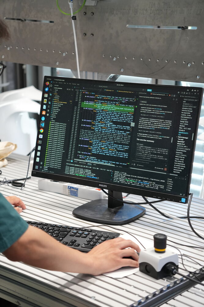 A builder writing robotics code next to a camera module on the bench
